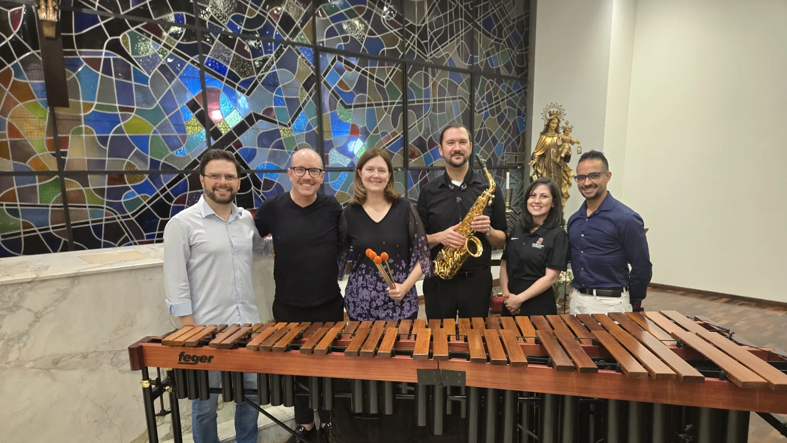 People standing behind a Marimba with a mosaic on the background