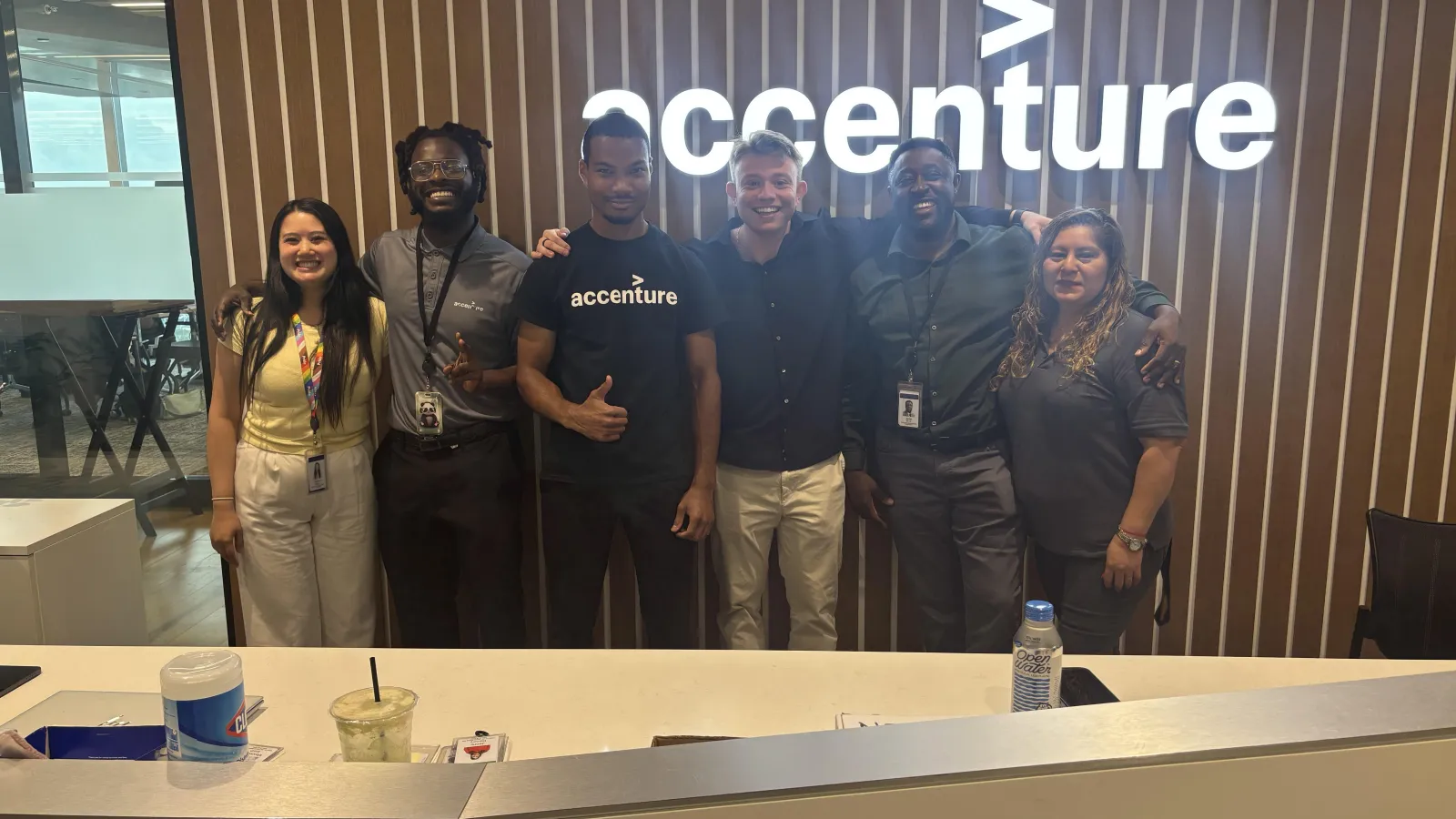 group of 6 people next to each other in front of sign that says Accenture