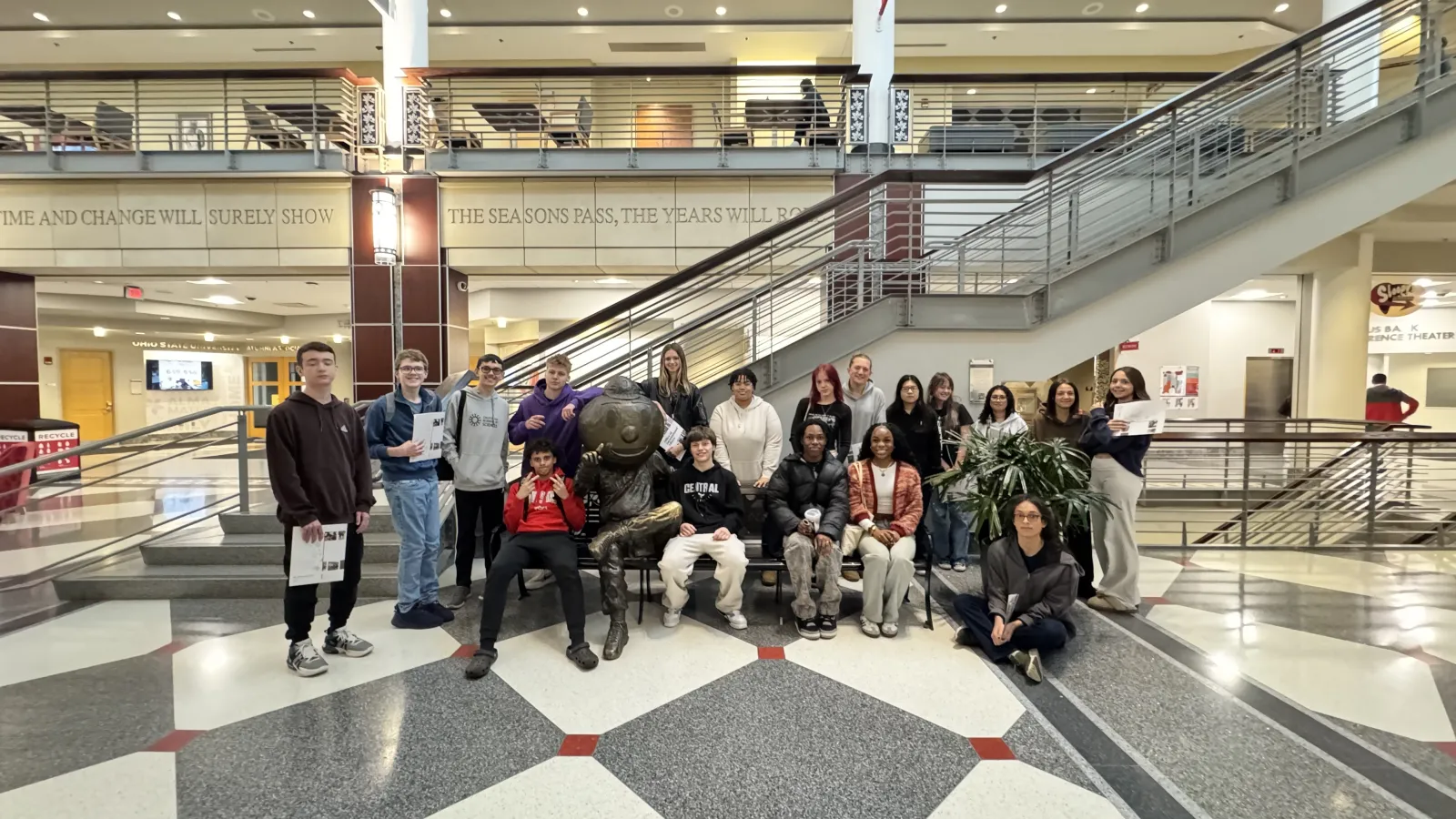 group of students sitting on a bench with Brutus statue