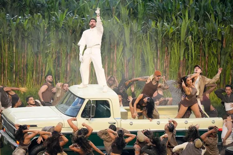 bad bunny in white on top of a truck with people dancing around it. Photo by Charlie Riedel - AP